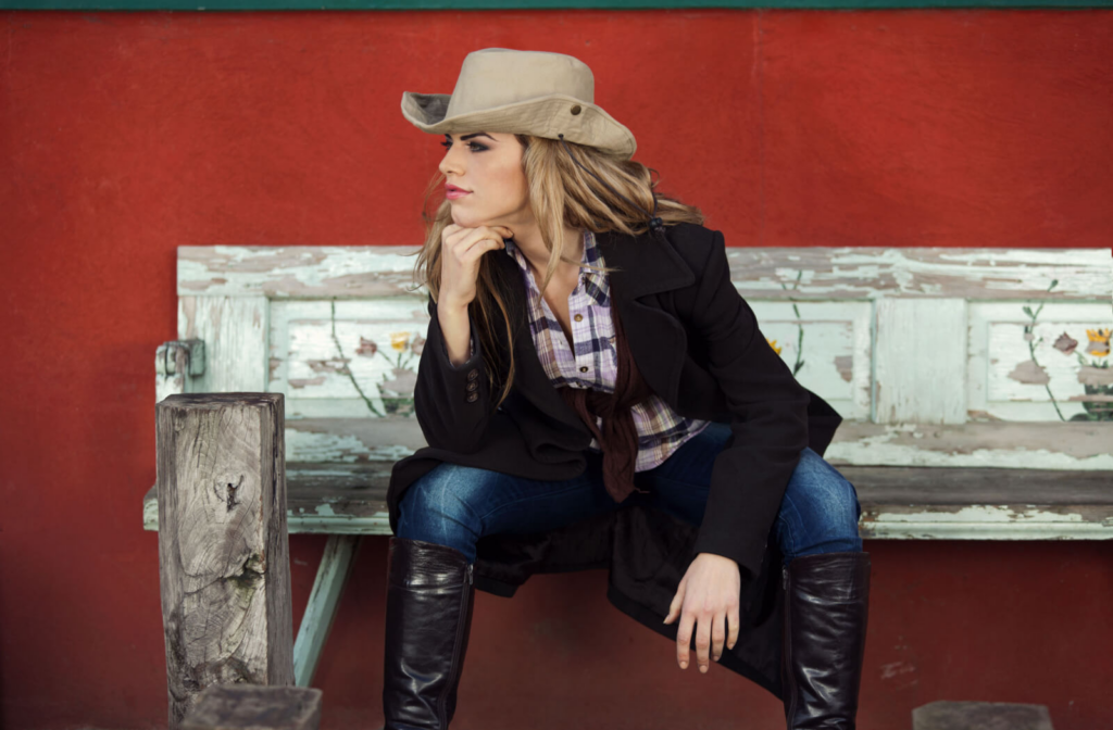 A woman in a cowboy hat and cowboy boots sitting on a wooden bench.