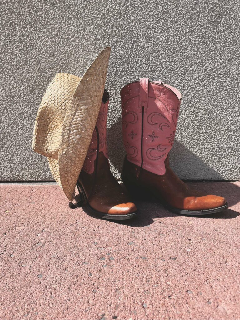 a pair of pink cowboy boots and a straw hat that can be purchased at peacock boutique for stampede