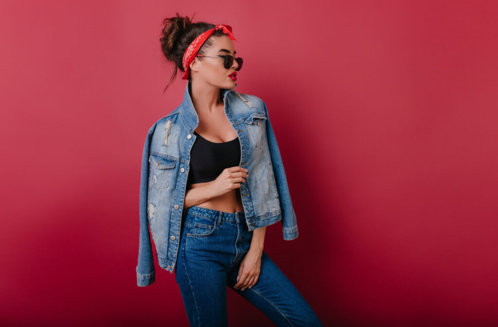 A stylish woman wearing black sunglasses, a red bandana, and denim on denim posing against a red background.