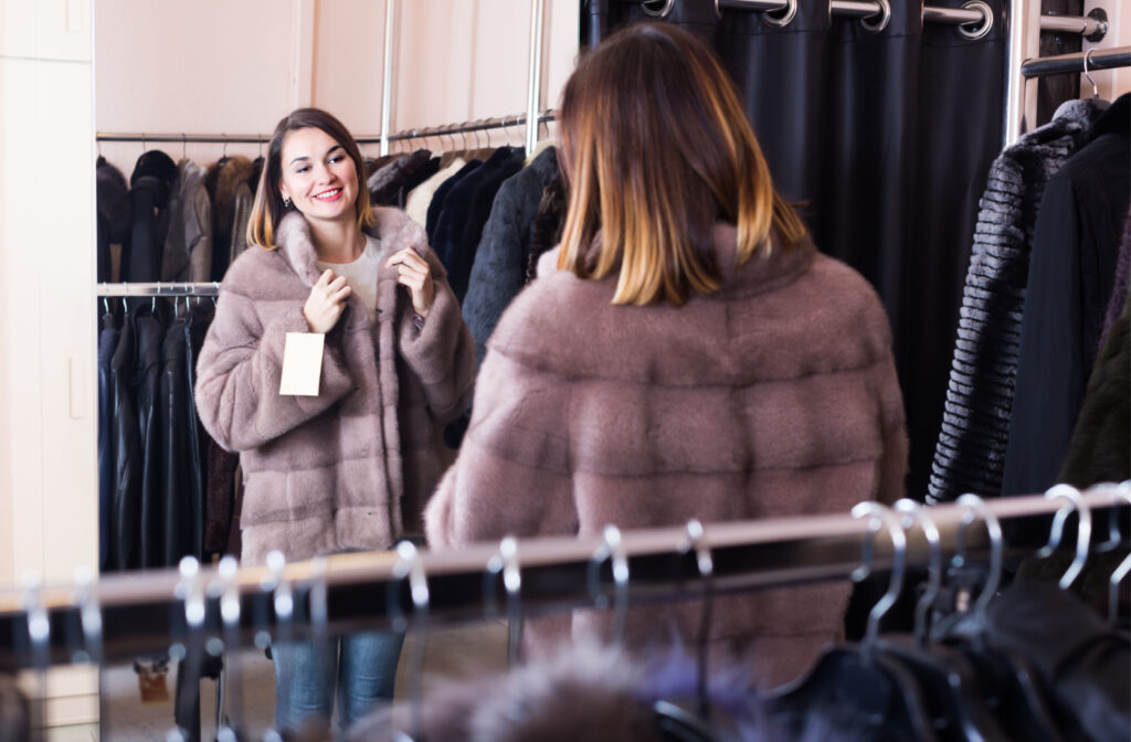 A woman looking in the mirror and trying on a fur coat in a boutique.