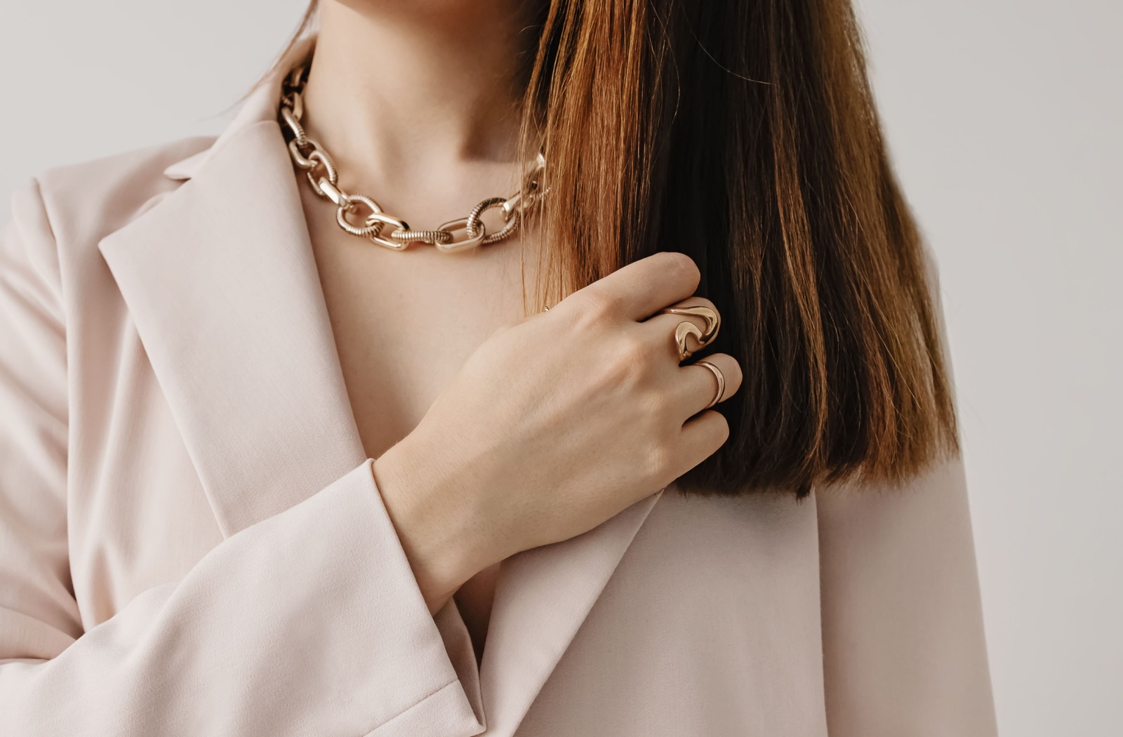 A close-up of a person wearing a beige blazer with gold accessories.