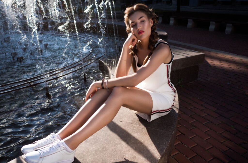 A stylish woman sits by a fountain, wearing trendy, slim sneakers.