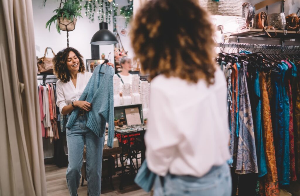 A person shopping at a local boutique holding a piece of knitwear against themselves in front of the mirror.