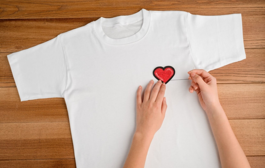 A person sews a red heart patch to an old t-shirt to give it a new life in their wardrobe.